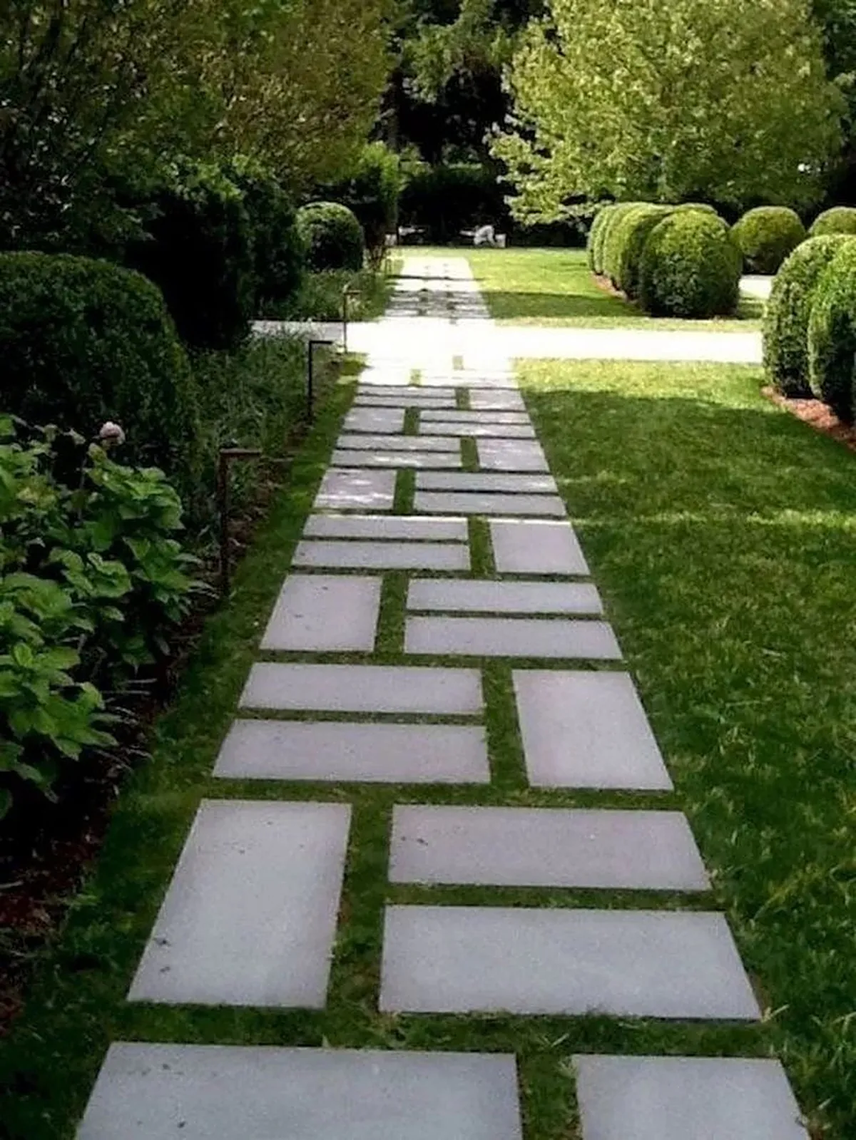 Caminho de placas de concreto assentadas sobre o gramado de um jardim arborizado