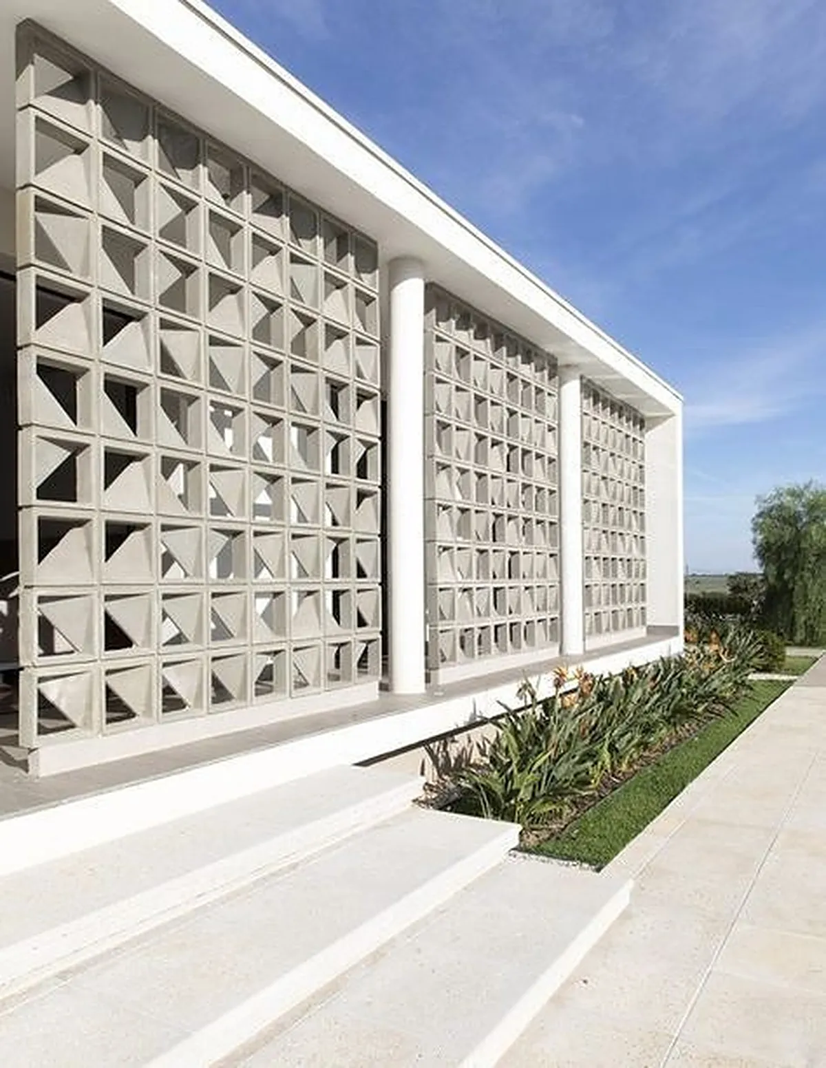Fachada branca com painéis de cobogó triângulo e jardim junto à calçada