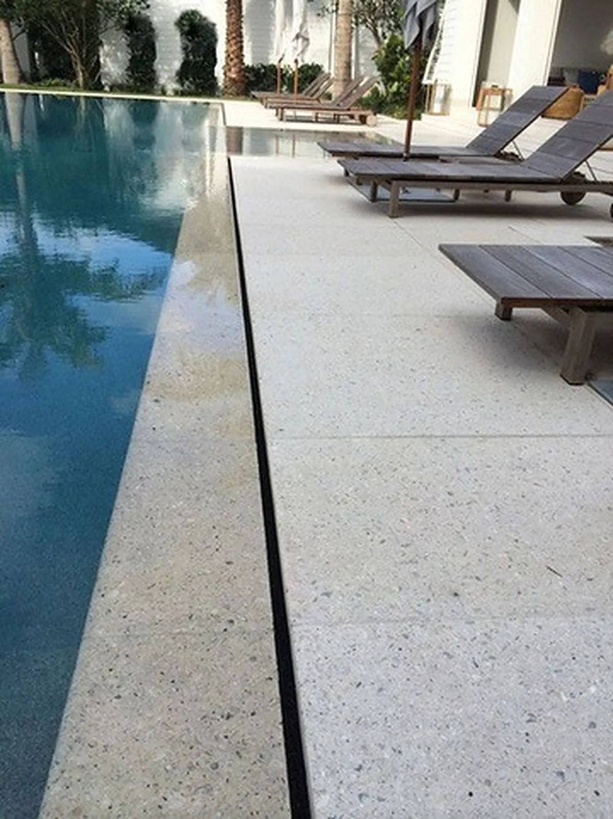 Borda atérmica clara acompanhando a lateral de uma piscina, com deck e espreguiçadeiras ao fundo